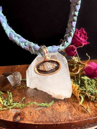 Necklace with braided cord and pendant on a crystal with flowers and moss in the background