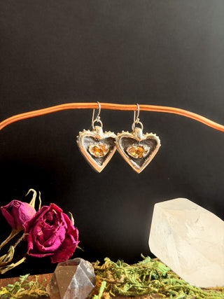 Heart-shaped earrings with embedded stones on a dark background with decorative elements.