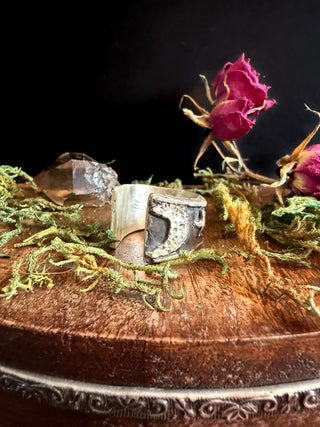 Silver ring with moon design on a wooden surface with a pink rose and greenery from Starwitch Metals