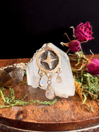Decorative star pendant with moonstone teardrop dangles on a crystal with dried flowers in the background designed by Starwitch Metals.